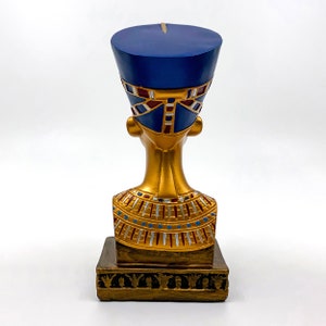 Peut inclure: Buste en or d'une reine &eacute;gyptienne portant une coiffe bleue avec des accents rouges et dor&eacute;s. La statue est sur une base dor&eacute;e avec des d&eacute;tails d&eacute;coratifs.
