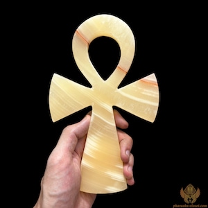 May include: A large, yellow-toned Ankh symbol made of polished onyx with red veins. The Ankh is a symbol of life and immortality in ancient Egyptian culture.