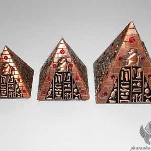May include: Three decorative metal pyramids with red jewels and hieroglyphics. The pyramids are different sizes and are arranged from smallest to largest.