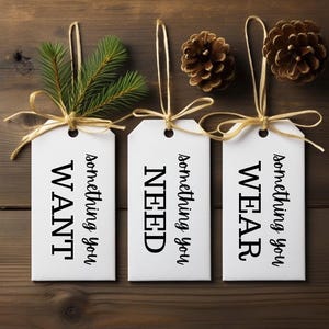 Peut inclure: Trois étiquettes cadeaux blanches avec de la ficelle. Les étiquettes portent les mots "something you WANT", "something you NEED" et "something you WEAR".