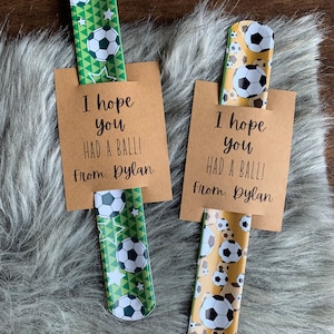 May include: Two brown cards with the text "I hope you had a ball! From: Dylan" on them. Each card has a green and white or yellow and white soccer ball patterned bookmark attached to it.
