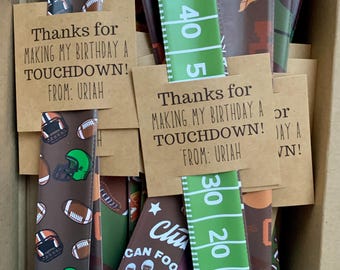 May include: A box of brown and green football-themed party favors. The favors are made of fabric and have a variety of designs, including footballs, helmets, and players. The favors are tied with brown twine and have a thank you tag that reads "Thanks for making my birthday a touchdown! From: Uriah".