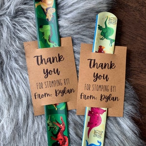 May include: Two brown thank you cards with the text "Thank you for stomping by! From: Dylan" and a dinosaur-themed ruler sticking out of the top of each card.