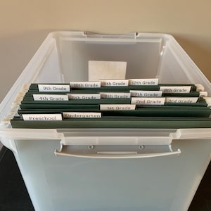 May include: A clear plastic storage bin with a handle, filled with green hanging file folders labelled with different grade levels: Preschool, Kindergarten, 1st Grade, 2nd Grade, 3rd Grade, 4th Grade, 5th Grade, 6th Grade, 7th Grade, 8th Grade, 9th Grade, 10th Grade, 11th Grade, and 12th Grade.