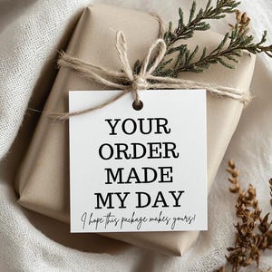 Puede incluir: Una etiqueta de regalo blanca con texto negro que dice "¡Tu pedido me ha alegrado el día! ¡Espero que este paquete te alegre el tuyo!" La etiqueta está atada con un cordel a una caja de regalo marrón envuelta en papel marrón.