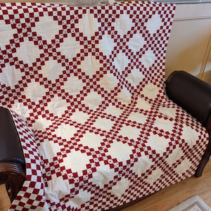 May include: A red and white checkered quilt with a floral pattern is draped over a brown leather armchair. The quilt is made of cotton fabric and has a traditional design.