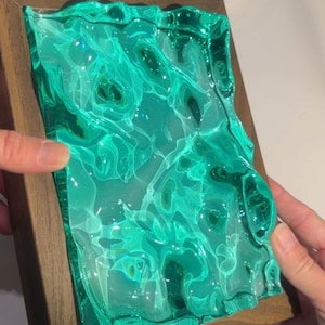 May include: A rectangular artwork featuring a vibrant, swirling green resin design set within a wooden frame. The resin has a translucent quality, with a marbled effect. The frame is a warm, natural wood tone.