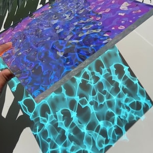 May include: A holographic iridescent sheet with a blue and purple abstract pattern. The sheet is casting a blue and green light pattern on a white surface.