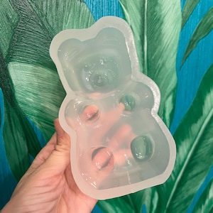 Puede incluir: Un molde de silicona transparente con forma de osito de goma. El molde tiene detalles, incluyendo la cara y la barriga del oso. El molde está diseñado para crear caramelos de goma u otras pequeñas golosinas.