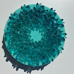Puede incluir: Un posavasos circular azul turquesa con un anillo de piezas de cristal azul turquesa alrededor del centro.