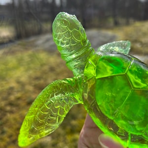 Puede incluir: Una figurita de tortuga marina de vidrio verde con caparazón y aletas detalladas.