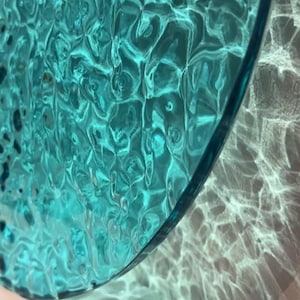 May include: A teal blue glass plate with a rippled texture. The plate is casting a shadow on a white surface.