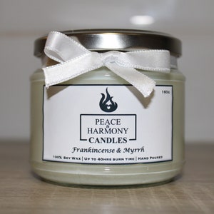 May include: A glass jar candle with a silver lid and a white ribbon tied around the top. The label reads "Peace & Harmony Candles" with "Frankincense & Myrrh" below. The candle is filled with a pale green wax.
