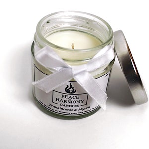 May include: A small glass jar candle with a white wax interior and a silver lid. The jar is adorned with a white ribbon and a label that reads "Peace Harmony Candles" with the scent "Frankincense & Myrrh".