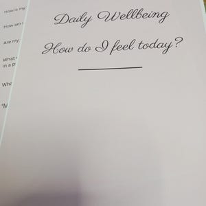 Op de afbeelding: Een lichtroze pagina uit een dagboek met de woorden "Daily Wellbeing" en de vraag "How do I feel today?" in sierlijke letters. De pagina bevat ook vragen als "How am I feeling today?" en "What's on my mind?" voor dagelijkse reflectie.