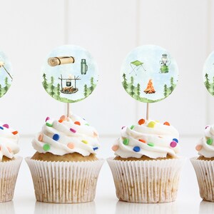 May include: Four cupcakes with white frosting and colorful sprinkles topped with round, illustrated camping-themed cupcake toppers. The toppers feature images of a backpack, a marshmallow on a stick, a sleeping bag, a thermos, a camping chair, a lantern, a campfire, and a tent.