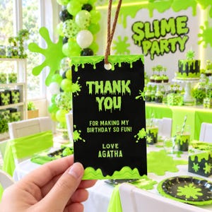 May include: A rectangular black gift tag with a lime green slime drip border and lime green text that reads THANK YOU FOR MAKING MY BIRTHDAY SO FUN! LOVE AGATHA. The tag features a hole at the top with a brown twine string attached for hanging.