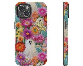 May include: A white iPhone 15 case with a colorful floral pattern and a white ghost with black eyes in the center.