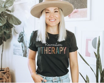 May include: A black t-shirt with the text "Recreation THERAPY" in colorful letters with a leopard print pattern.