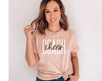 May include: A light pink t-shirt with the text "COACH cheer" in white and black lettering.