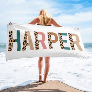 May include: A white beach towel with the name "HARPER" printed in large letters. Each letter is decorated with a brown, orange, and teal leopard print pattern.