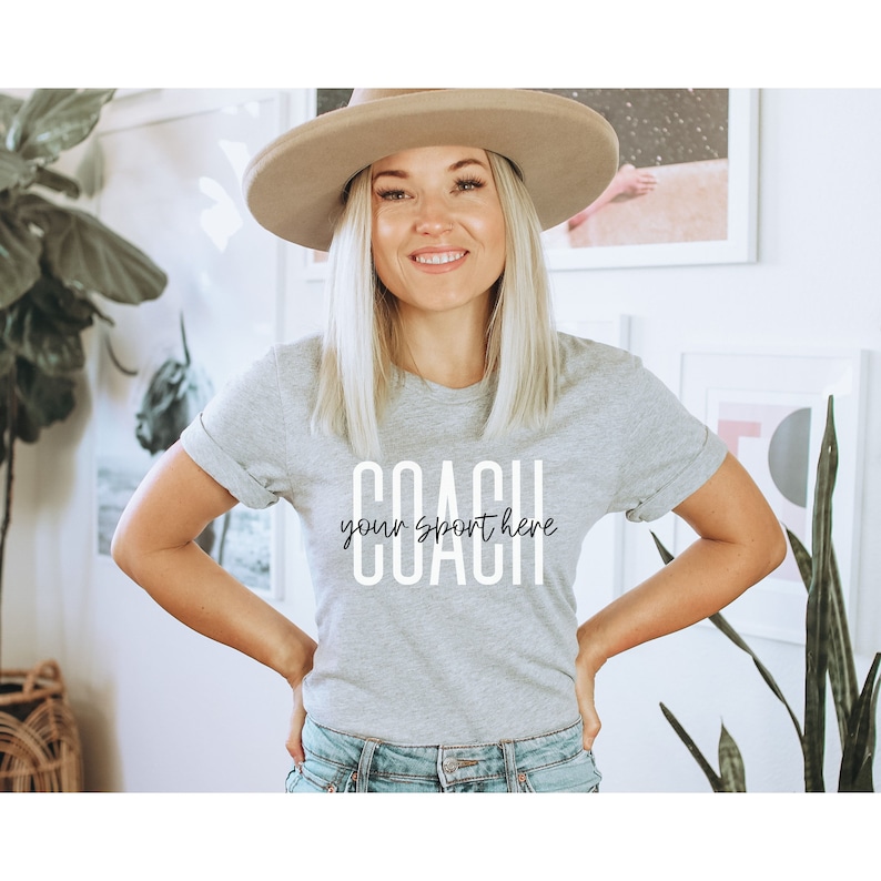 Op de afbeelding: Een grijs T-shirt met de tekst "COACH your sport here" in wit gedrukt.