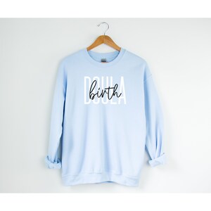 K&ouml;nnte beinhalten: Ein hellblauer Pullover mit dem Aufdruck "Doula birth" in Wei&szlig; auf der Vorderseite.