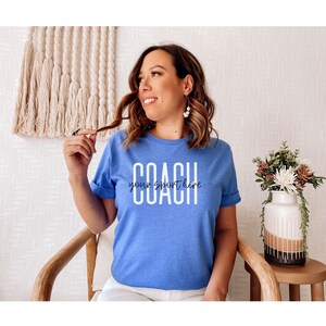 Op de afbeelding: Een blauw t-shirt met witte tekst die "COACH your sport here" luidt.