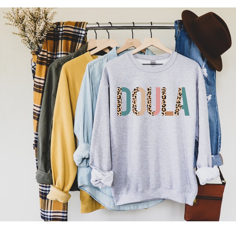 May include: A gray sweatshirt with the word "DOULA" printed in colorful letters with a leopard print pattern. The letters are outlined in teal, pink, and brown.