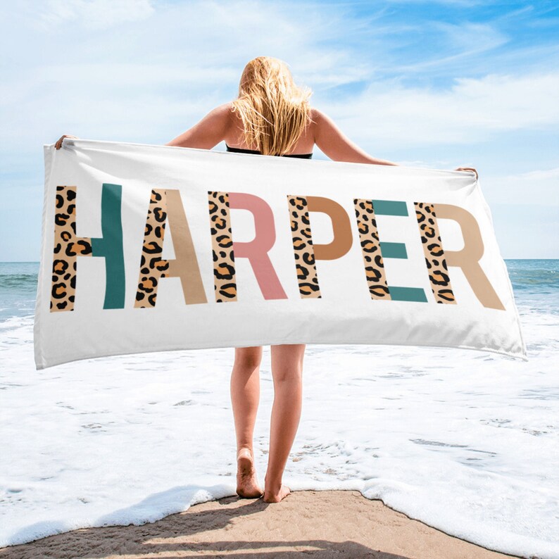 May include: A white beach towel with the name "HARPER" printed in large letters. Each letter is decorated with a brown, orange, and teal leopard print pattern.