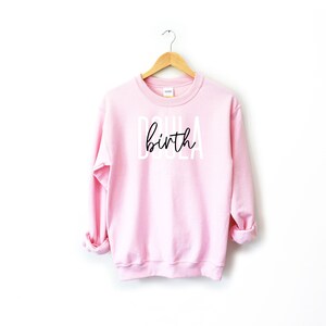 K&ouml;nnte beinhalten: Rosafarbener Pullover mit dem Text "Doula birth" in wei&szlig;en Buchstaben mit schwarzer Schrift.