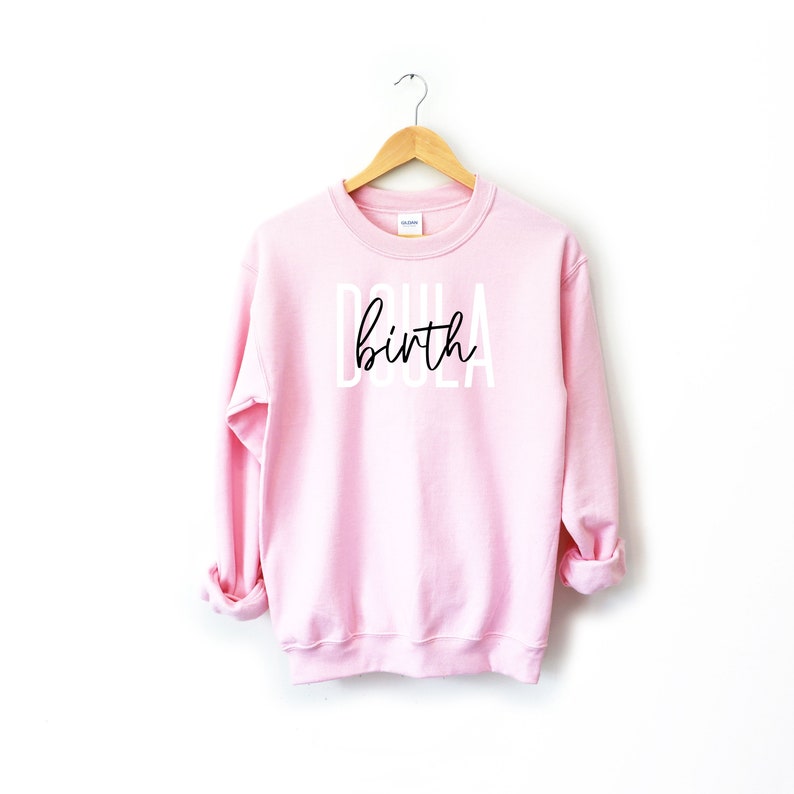 K&ouml;nnte beinhalten: Rosafarbener Pullover mit dem Text "Doula birth" in wei&szlig;en Buchstaben mit schwarzer Schrift.