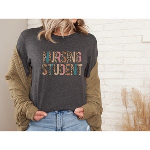 May include: A dark gray t-shirt with the words "Nursing Student" printed in colorful letters with a leopard print pattern.