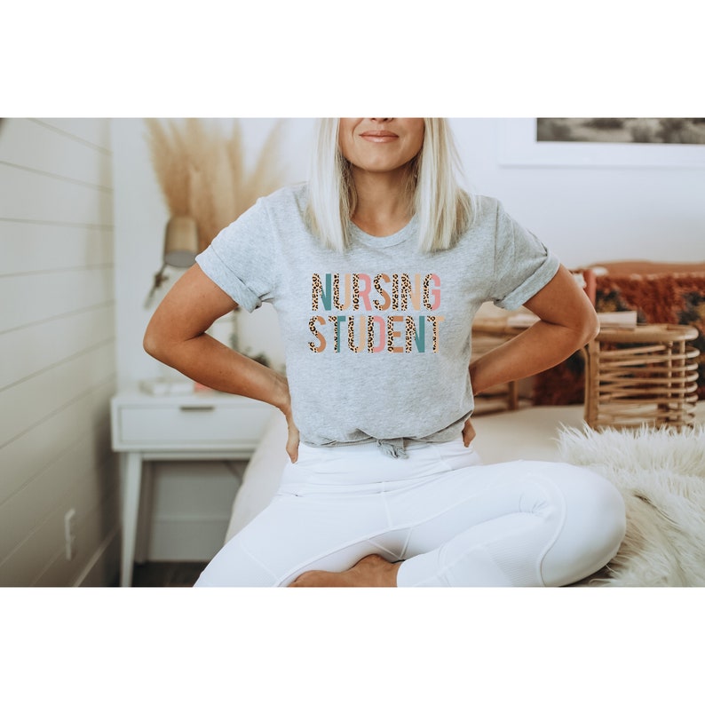 May include: A grey t-shirt with the words "Nursing Student" printed in colorful letters with a leopard print pattern.