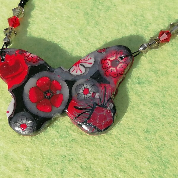 Collier papillon en pâte polymère fleurs en millefiori avec differents tons de rouges, gris sur fond noir, paillettes et perles.