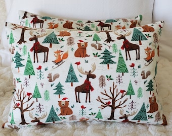May include: Two rectangular cushions with a white background featuring a repeating pattern of woodland creatures, trees, and red accents. The animals include moose, bears, foxes, and squirrels. The trees are green and brown.