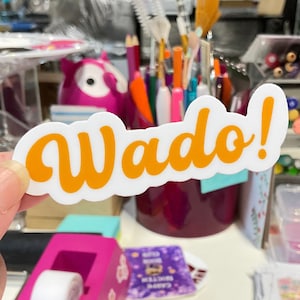 May include: A white sticker with the word "Wado!" written in orange cursive lettering.