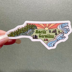 North Carolina sticker featuring Charlotte, Raleigh/Durham area, mountains, beaches, sunshine, and farms. Sticker is in the shape of NC with a white offset.