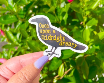 May include: A black crow sticker with the text "Once upon a midnight dreary" in yellow. The sticker is being held in a hand with purple nail polish.