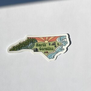 North Carolina sticker featuring Charlotte, Raleigh/Durham area, mountains, beaches, sunshine, and farms. Sticker is in the shape of NC with a white offset.