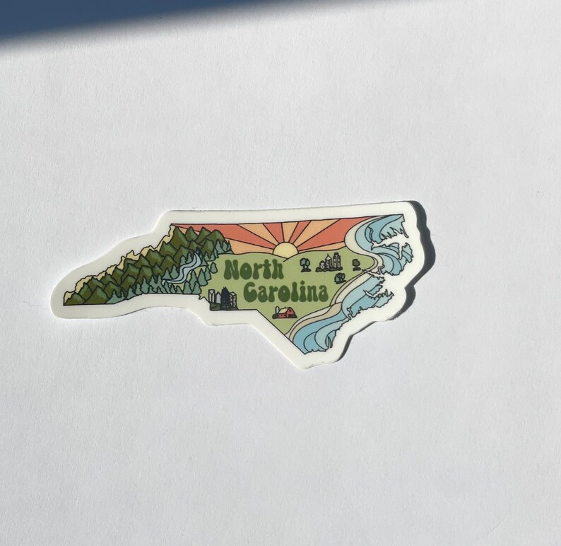 North Carolina sticker featuring Charlotte, Raleigh/Durham area, mountains, beaches, sunshine, and farms. Sticker is in the shape of NC with a white offset.