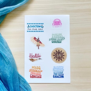 May include: A white sticker sheet featuring various designs including a Choctaw logo, a pink car, a person in traditional regalia, a sun emblem, and text graphics reading Halito, Dancing 3 Sisters, Beads, Stickball, Powwow, Baskets, Frybread, and Pottery.