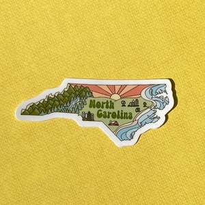 North Carolina sticker featuring Charlotte, Raleigh/Durham area, mountains, beaches, sunshine, and farms. Sticker is in the shape of NC with a white offset.