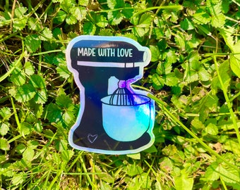 May include: A black and white sticker of a stand mixer with the text "MADE WITH LOVE" on it. The sticker is on a green grassy background.