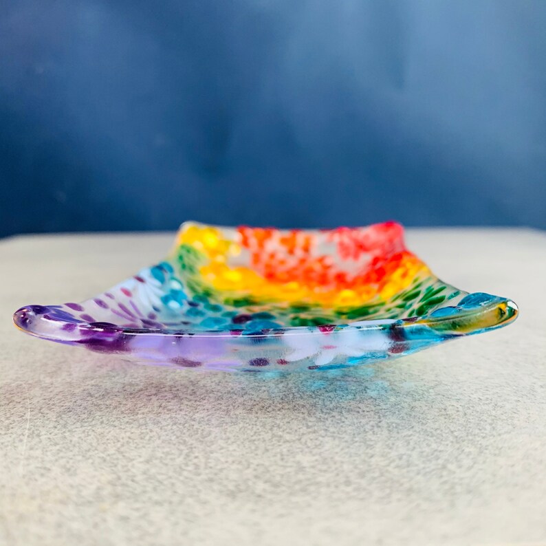 Puede incluir: Un plato de vidrio con forma de arco&iacute;ris con un patr&oacute;n moteado. El plato es transparente y tiene una ligera curva.