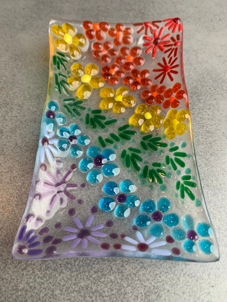 Puede incluir: Un plato de vidrio transparente con un dise&ntilde;o floral de arco&iacute;ris. El plato est&aacute; decorado con peque&ntilde;as flores y hojas de vidrio de colores.