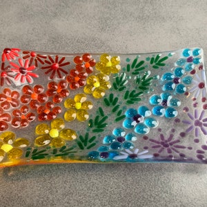 Puede incluir: Un plato rectangular de vidrio con un dise&ntilde;o de arco&iacute;ris de flores y hojas. El plato est&aacute; hecho de vidrio transparente y tiene una superficie texturizada.