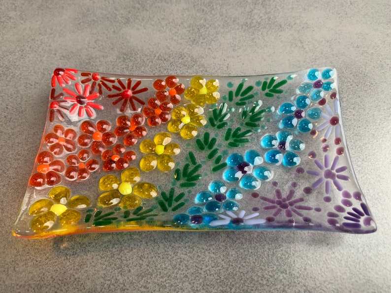 Puede incluir: Un plato rectangular de vidrio con un dise&ntilde;o de arco&iacute;ris de flores y hojas. El plato est&aacute; hecho de vidrio transparente y tiene una superficie texturizada.