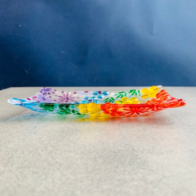 Puede incluir: Un plato de vidrio transparente con un dise&ntilde;o de arco&iacute;ris. El plato est&aacute; decorado con flores y puntos de colores.