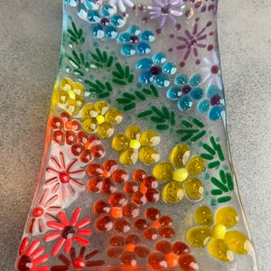 Puede incluir: Un plato de vidrio transparente decorado con peque&ntilde;as flores de vidrio en tonos de rojo, naranja, amarillo, verde, azul y morado.